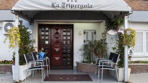 Entrada de hotel con una puerta de madera oscura, un toldo cubierto y dos sillas blancas afuera.