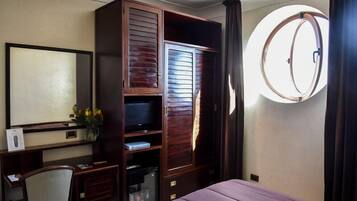 Une chambre d’hôtel comprenant un lit, un bureau avec une chaise, une armoire, un téléviseur et une fenêtre ronde.
