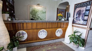 Una recepción de hotel con un mostrador de madera, tres placas circulares, un tapete de bienvenida y una foto enmarcada de un edificio.