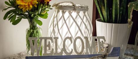 A welcome sign with a nautical theme, including a boat and rope details, next to a vase with flowers and a potted plant.