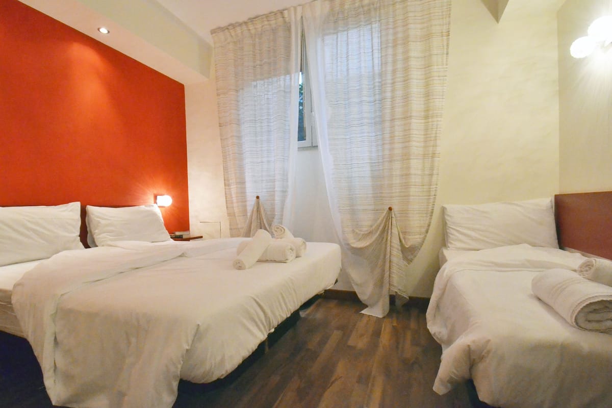 A hotel room with two beds, a wooden floor, and a red accent wall.