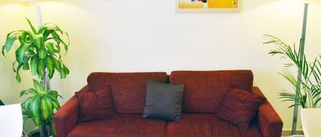 A red sofa with a pillow, two potted plants, and two abstract paintings on the wall.