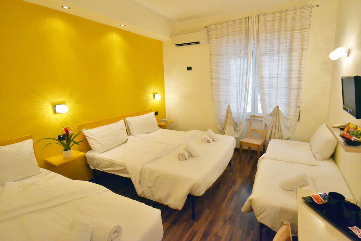A hotel room with two beds, a sofa, a TV, and a small table with a remote control.