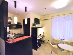 A compact kitchen with a red countertop, a dining area with a small table and chairs, and a living space with a TV and air conditioning unit. - Holiday a San Pietro (Rome)