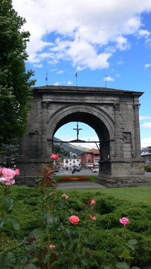 A stone archway with a cross at the top, surrounded by greenery and flowers.