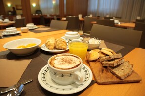A breakfast setting with croissants, a cup of coffee, orange juice, and bread on a wooden board.