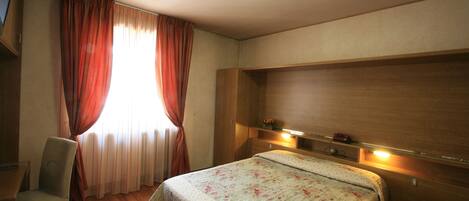 A bedroom with a bed, a chair, a desk, and a window with curtains.
