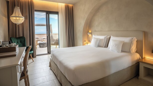 Ein Hotelzimmer mit einem großen Bett, einem Schreibtisch, einem Stuhl und Meerblick durch eine Schiebetür.