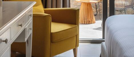 A hotel room with a bed, a yellow armchair, a white dresser, and a wicker chair outside.
