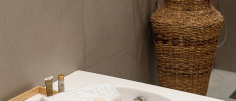 A bathroom with a white bathtub, a wooden tray with toiletries, and a wicker vase with flowers.
