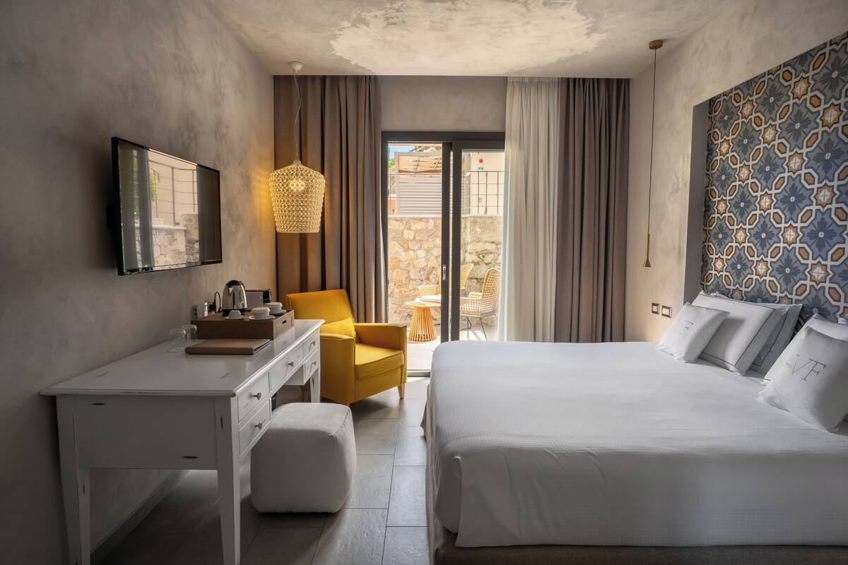 Une chambre d’hôtel avec un lit, un bureau, une chaise, une petite table et un balcon avec vue.