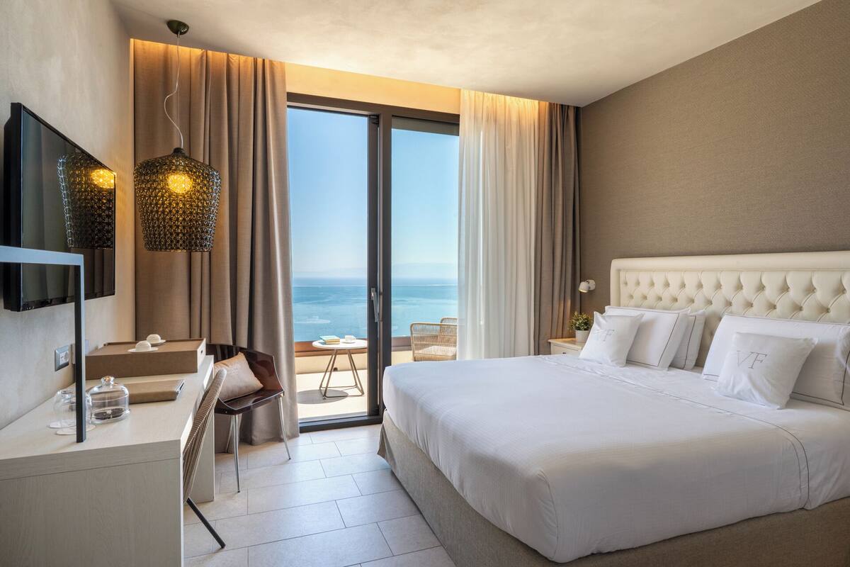 Une chambre d’hôtel avec un grand lit, une télévision, un bureau avec une chaise et une vue sur l’océan.