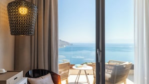 A hotel room with a bed, a desk, a chair, and a balcony with a view of the sea. - Villa Fiorita Boutique Hotel (Taormina)