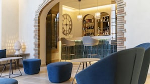 A modern lounge area with blue seating, a bar with shelves of bottles, and a large wall clock. - Villa Fiorita Boutique Hotel (Taormina)