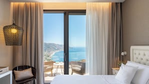 A hotel room with a large bed, a desk, a chair, and a view of the sea. - Villa Fiorita Boutique Hotel (Taormina)