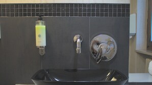 Un lavabo noir, de type « vessel », avec un distributeur de savon et un robinet, le tout posé sur un plan de travail blanc.