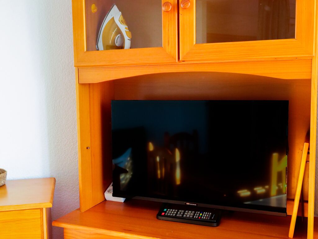 Un mueble bajo de madera para televisor con un televisor de pantalla plana, un control remoto y un estante pequeño con un objeto decorativo.