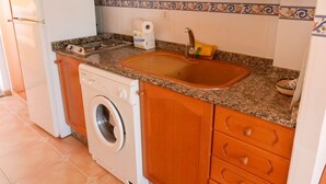 A compact kitchen with a washing machine, a sink, and wooden cabinets. - Kione Anamar (Alcala de Xivert)