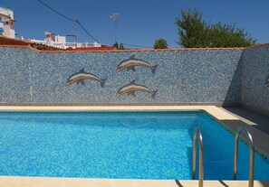 Une piscine dont le mur est décoré de mosaïques représentant des dauphins et qui est équipée de rampes métalliques.