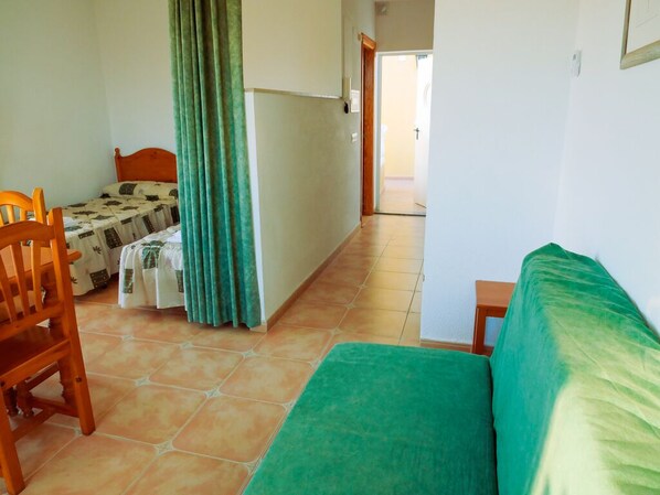 A room with a bed, a chair, a small table, and a curtain.