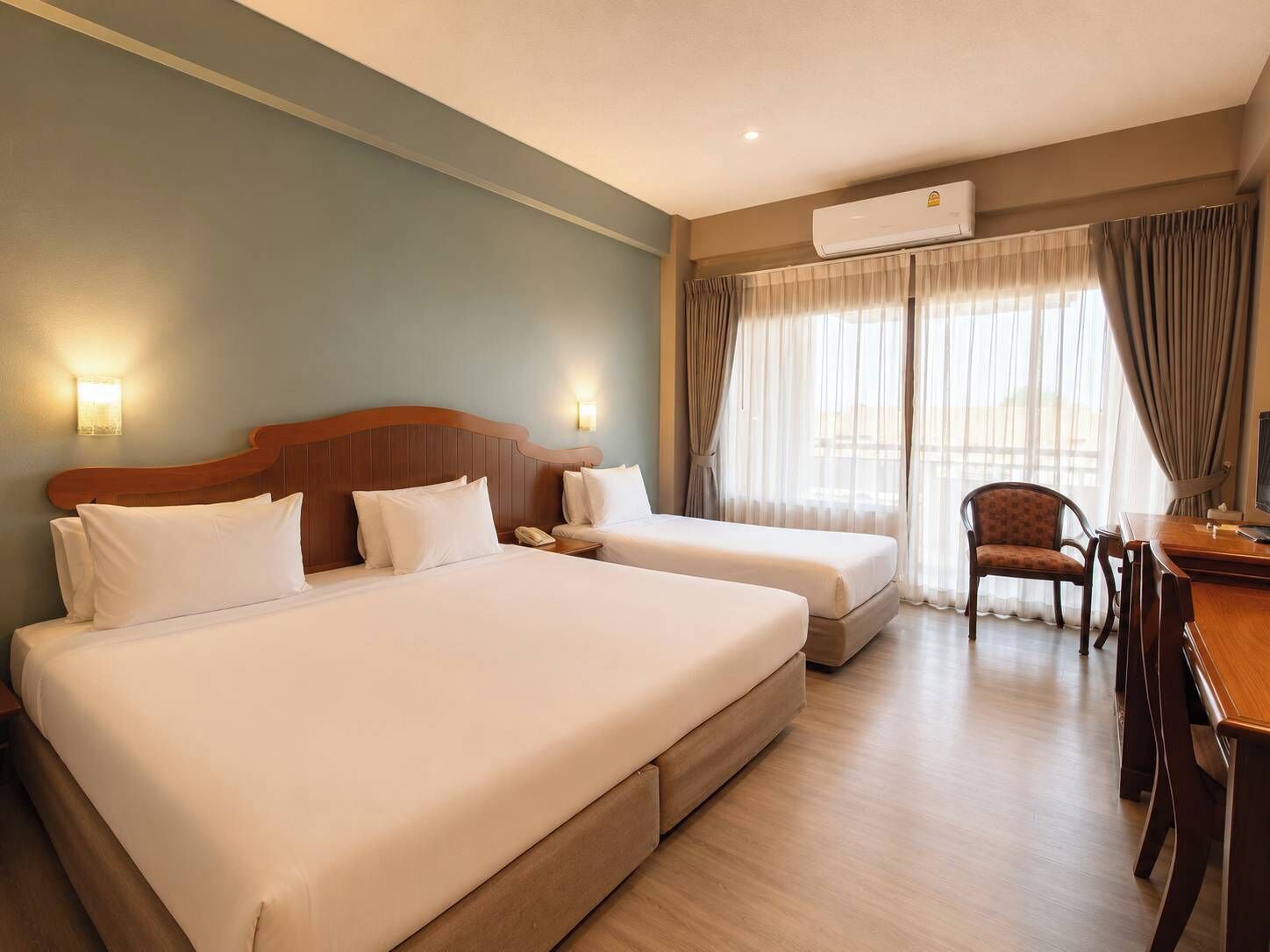 Een hotelkamer met twee bedden, een bureau, een stoel, een airconditioner en een raam met gordijnen.