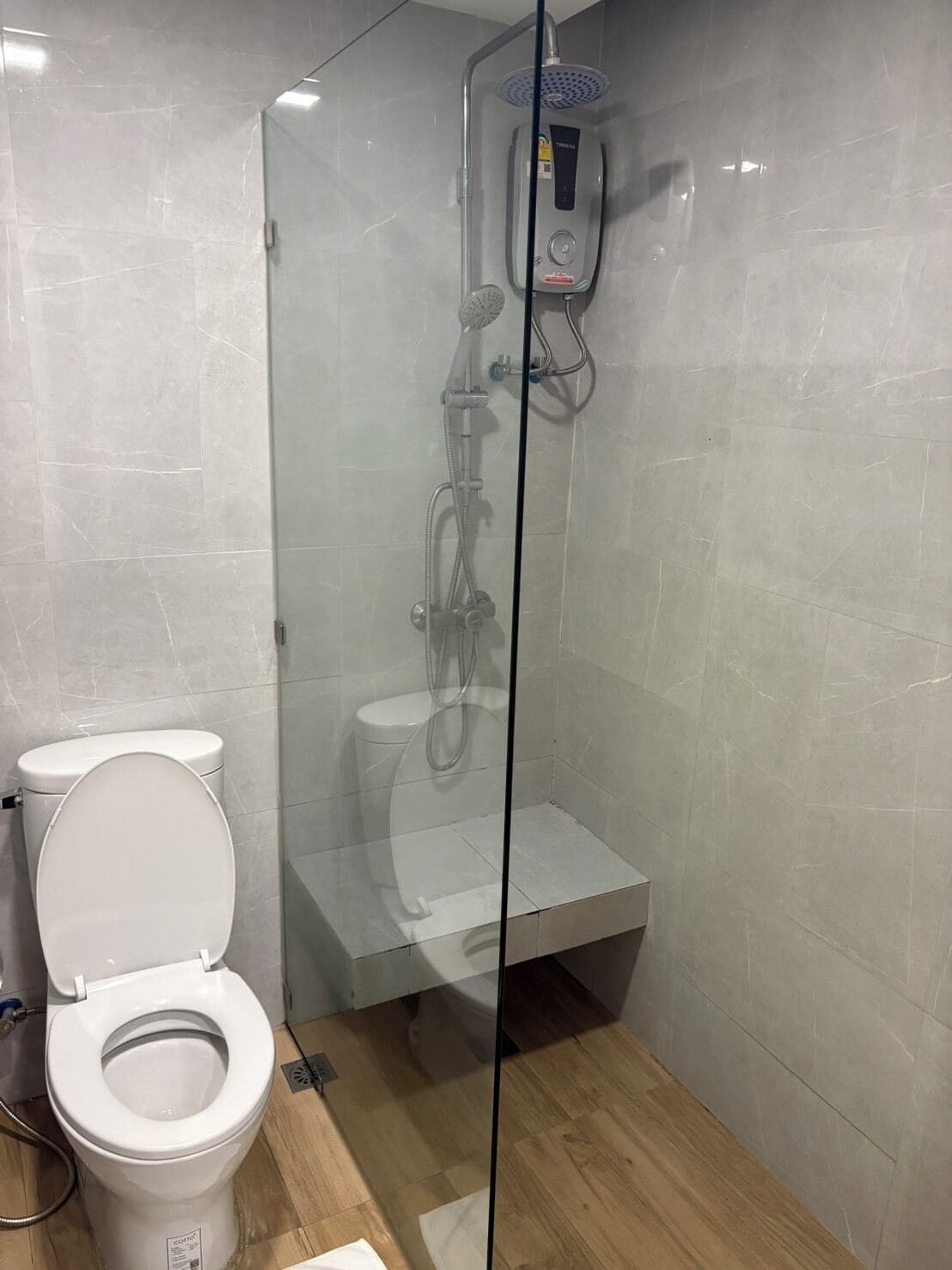 A modern bathroom with a glass-enclosed shower, a toilet, and a visible water heater.