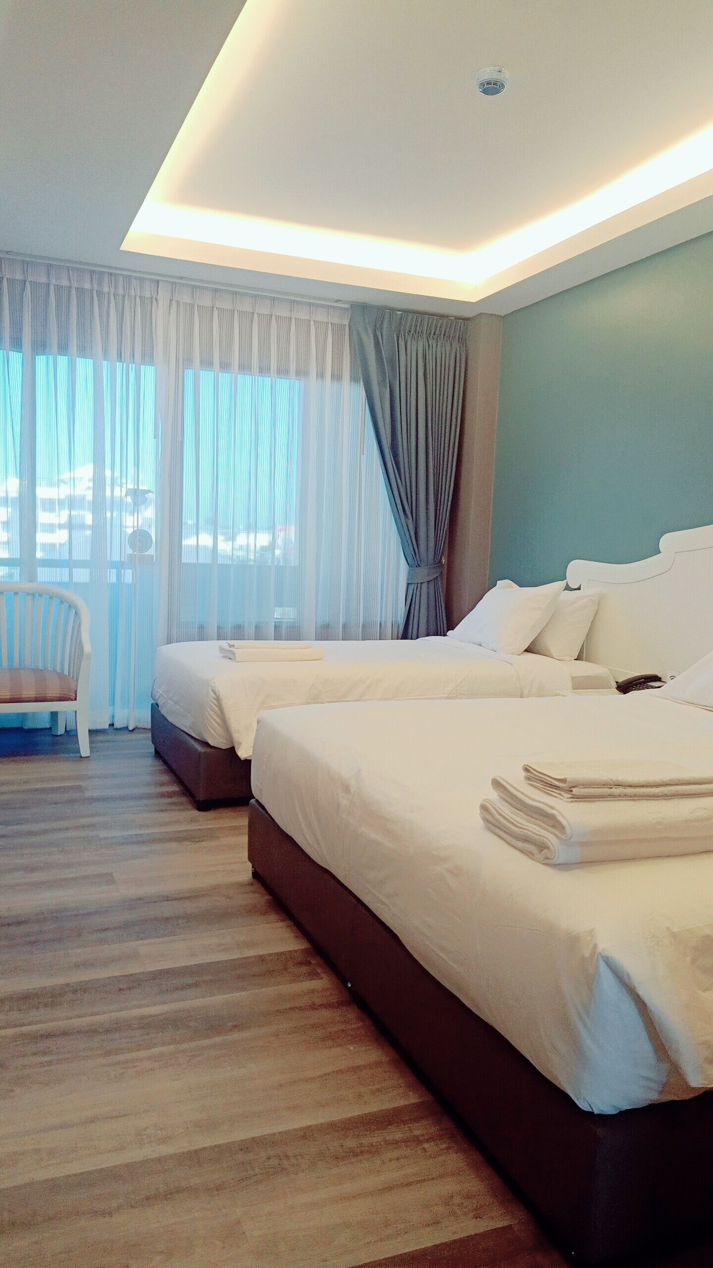 A hotel room with two beds, a chair, and a view of the outdoors.