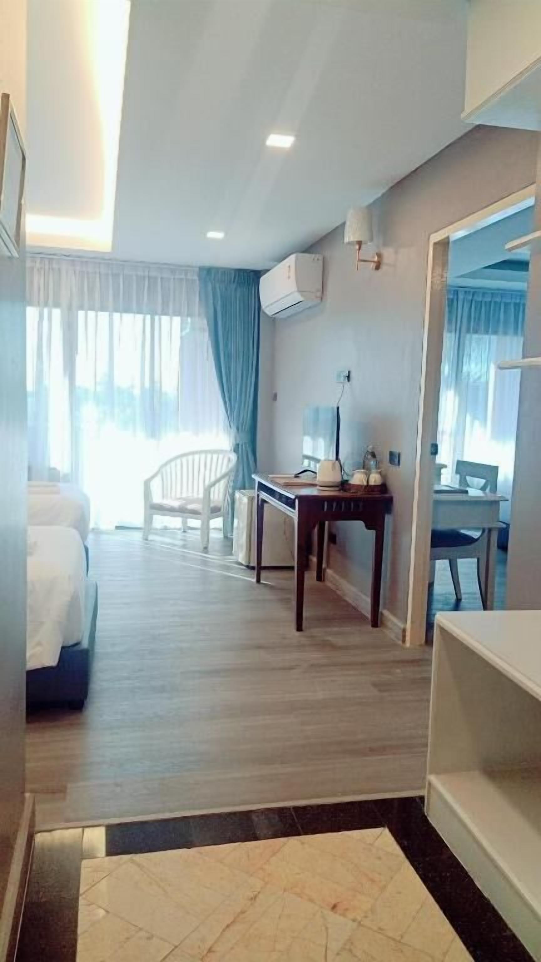 A hotel room with a bed, a desk, a chair, and a small table with a lamp.