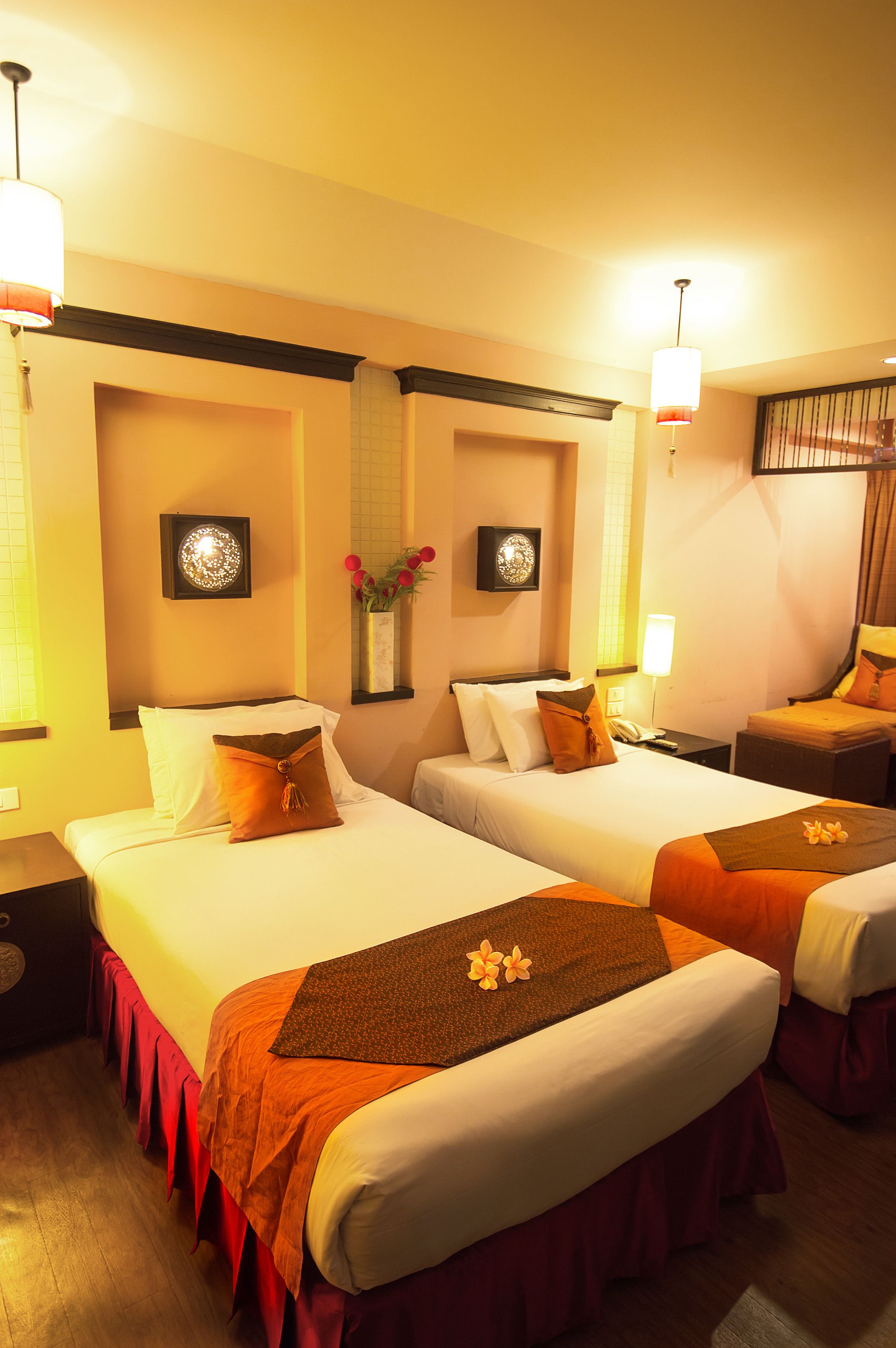 A hotel room with two beds, each with a red and white bedspread, a nightstand with a lamp, and a wall-mounted decorative item.