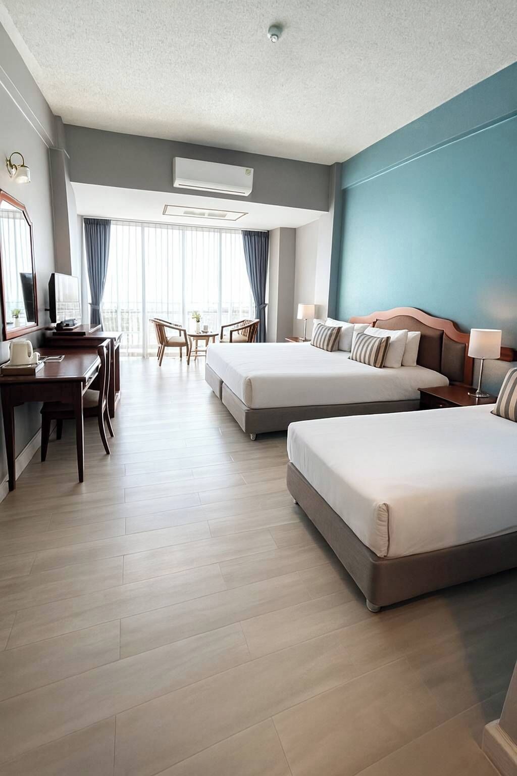 A hotel room with two beds, a desk, a chair, and a dining area with a view.