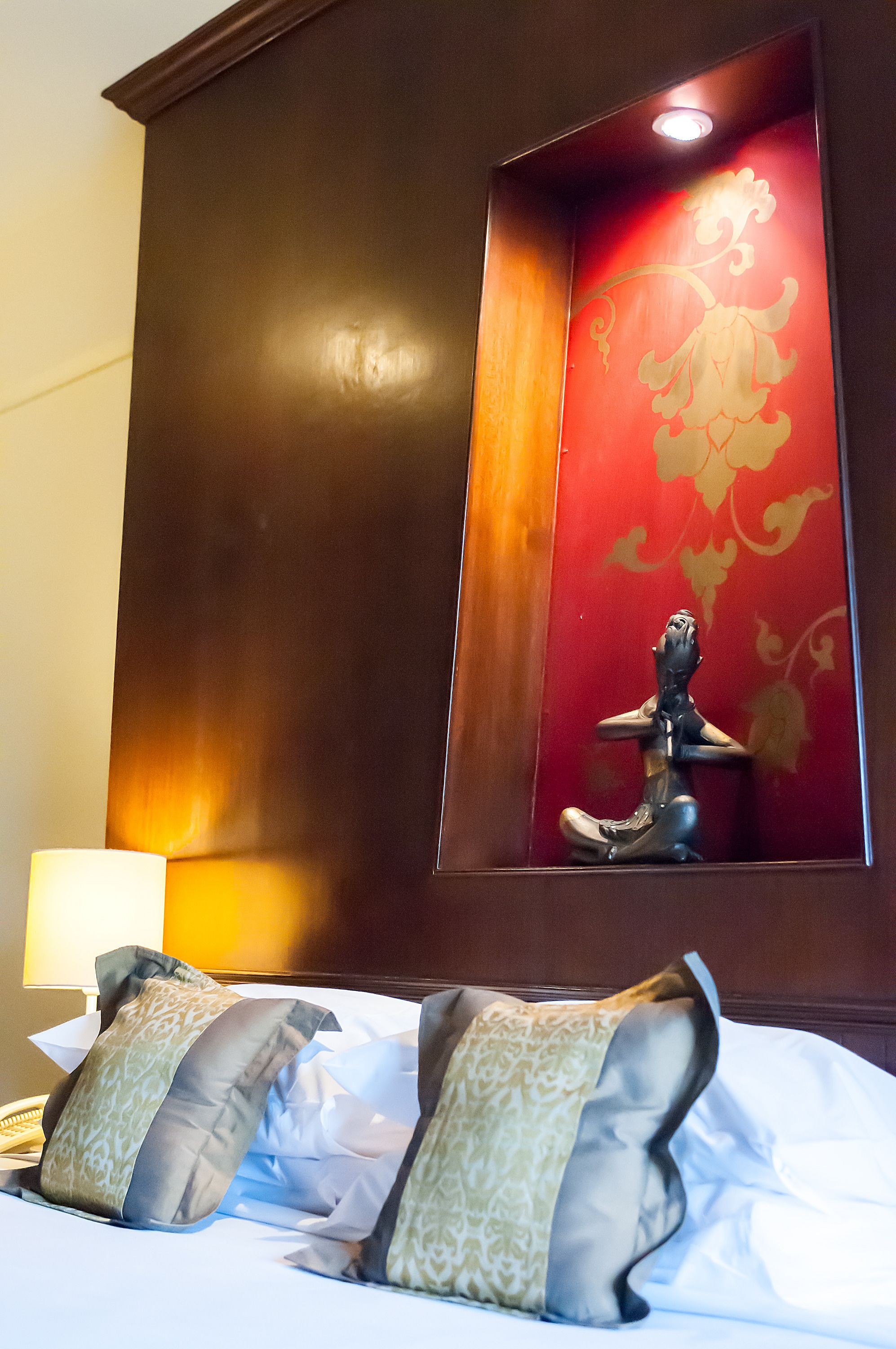 A hotel room with a bed, pillows, a nightstand, and a decorative wall panel.