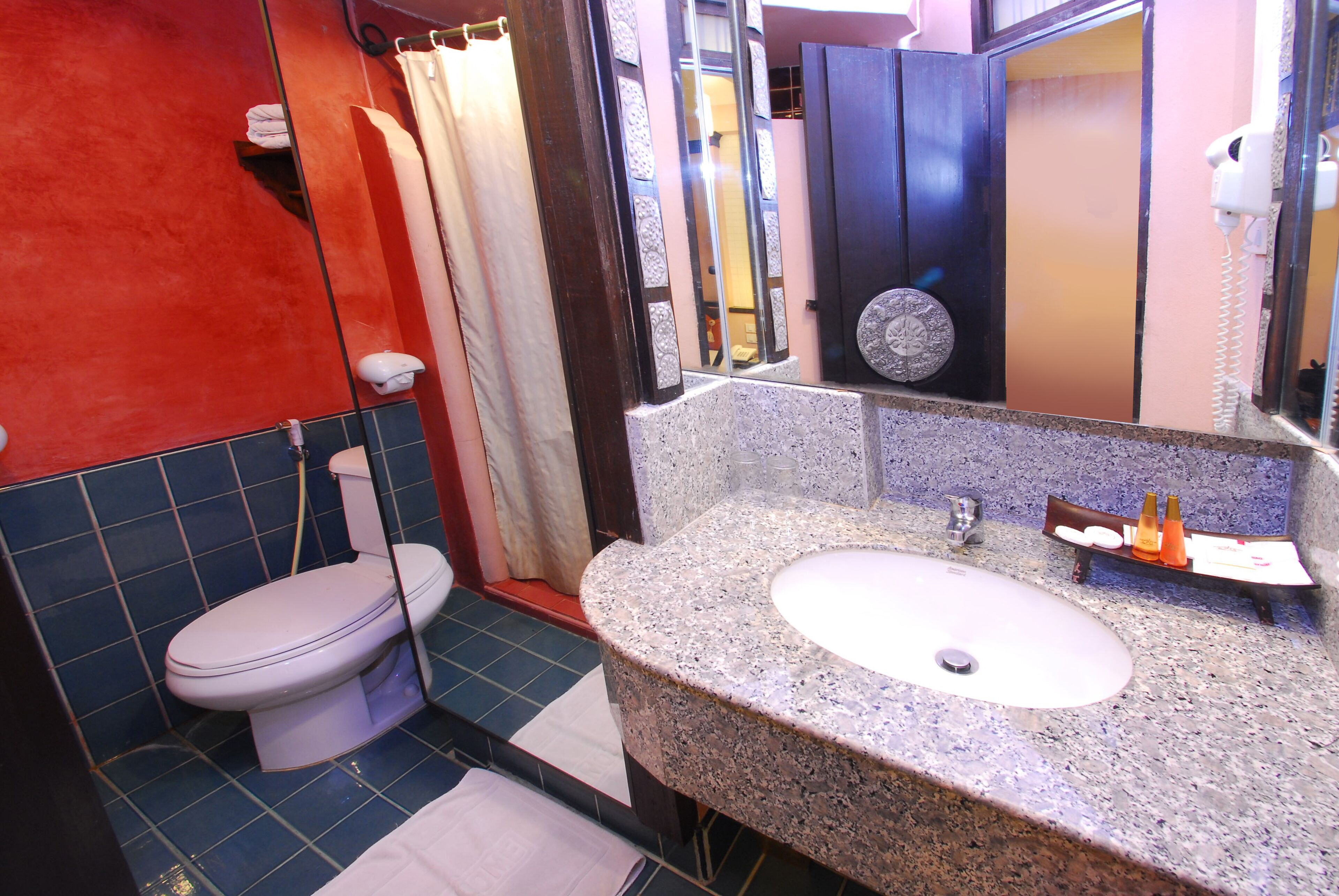 Un baño con inodoro blanco, lavamanos de granito, espejo y zona de ducha.
