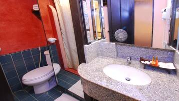 Un baño con inodoro blanco, lavamanos de granito, espejo y zona de ducha.
