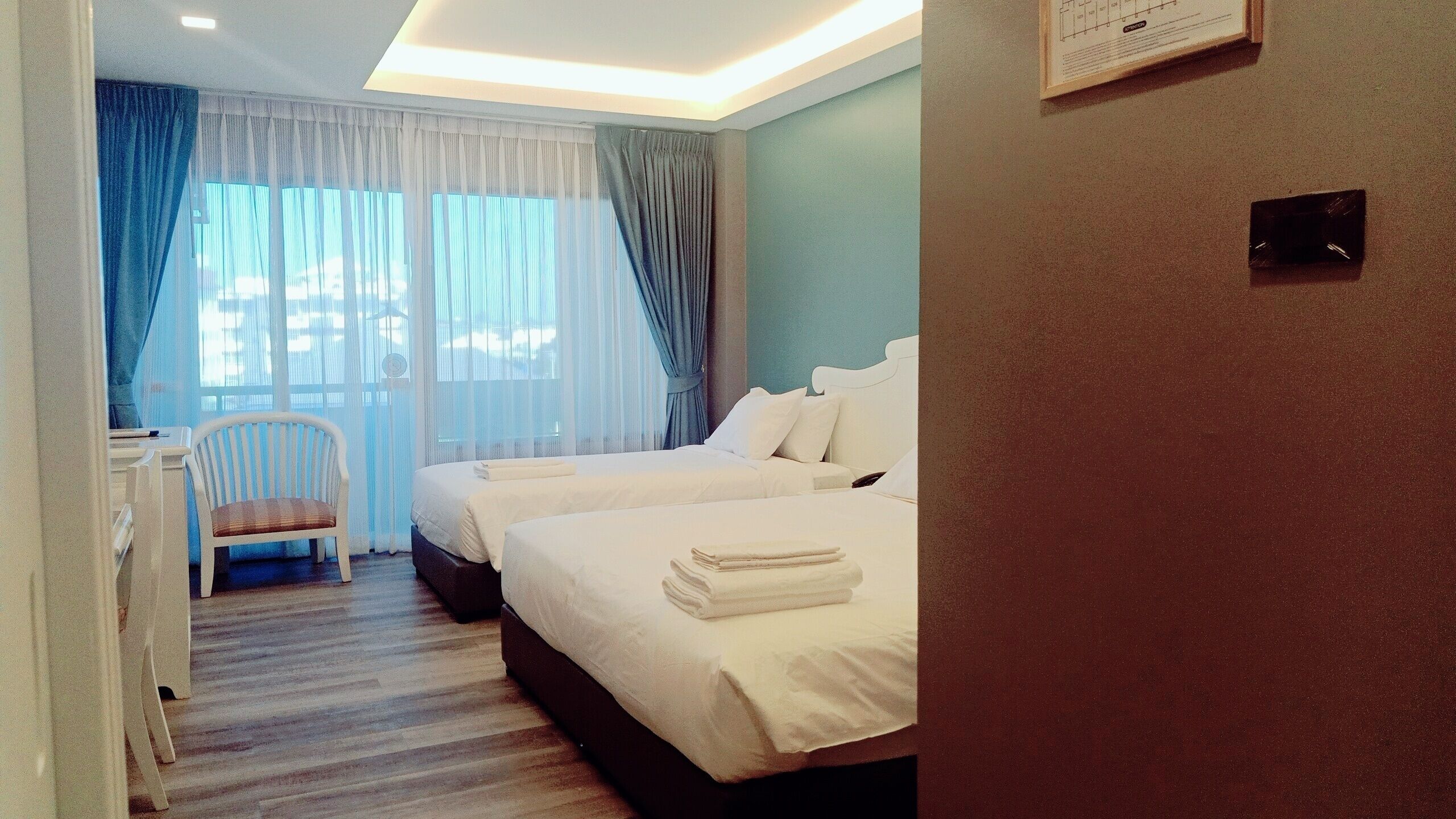 A hotel room with two beds, a chair, a desk, and a window with curtains.