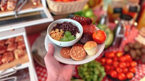 A hand holding a plate with various food items including cookies, a bowl of grapes, and a muffin. - Hotel Merlini (Florence)