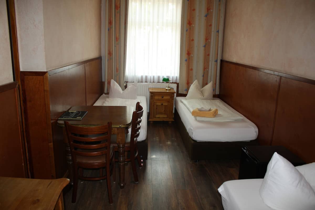 Una habitación de hotel compacta con dos camas individuales, una mesa de madera y una silla.