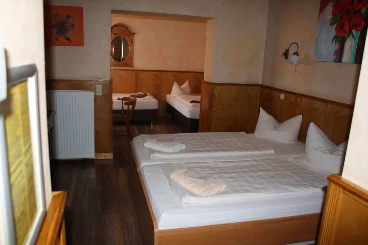 Habitación de hotel con dos camas individuales, cabecera de madera, radiador, una silla y un cuadro en la pared.