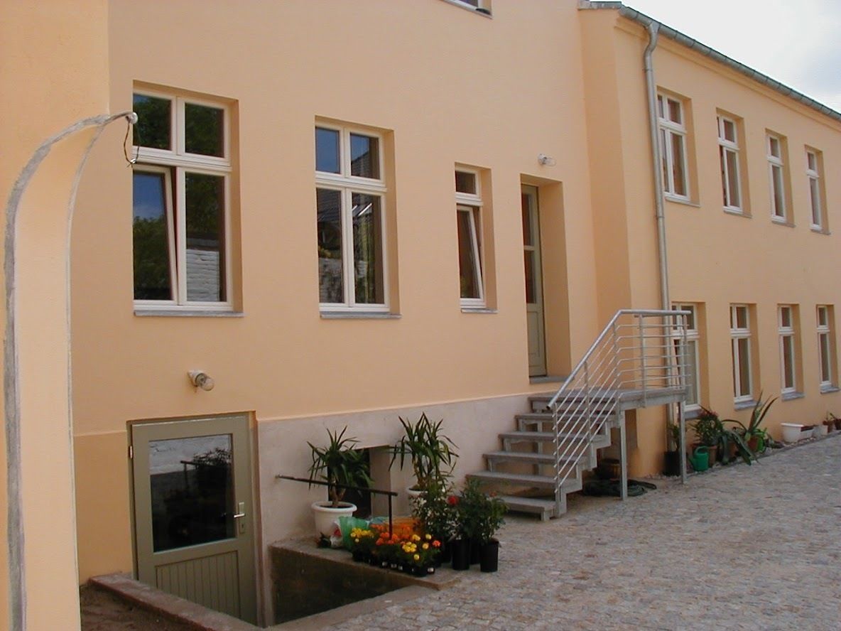 En bygning med gul facade, mange vinduer, en trappe og plantekasser.