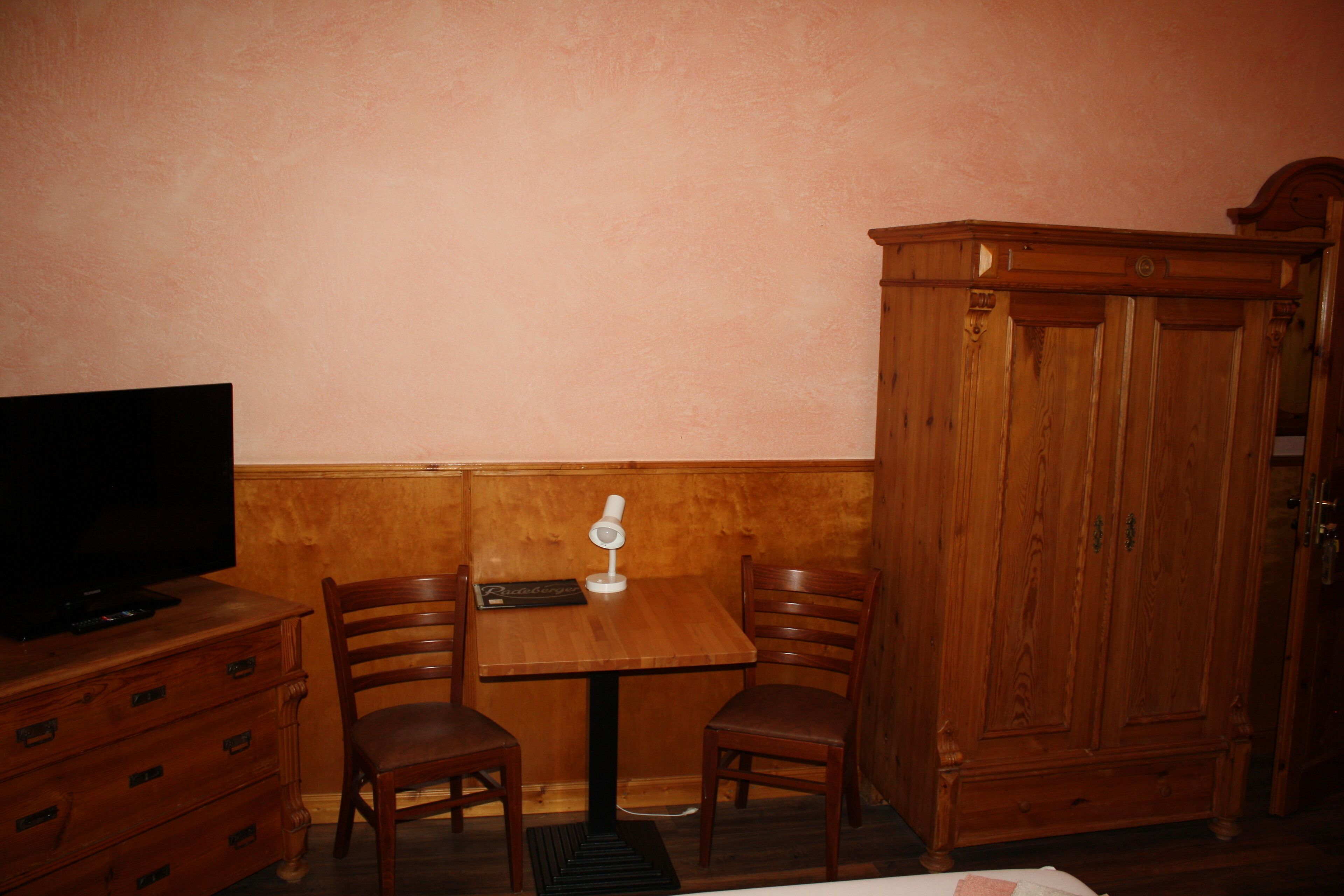 A room with a wooden cabinet, a television on a dresser, and two chairs around a small table.