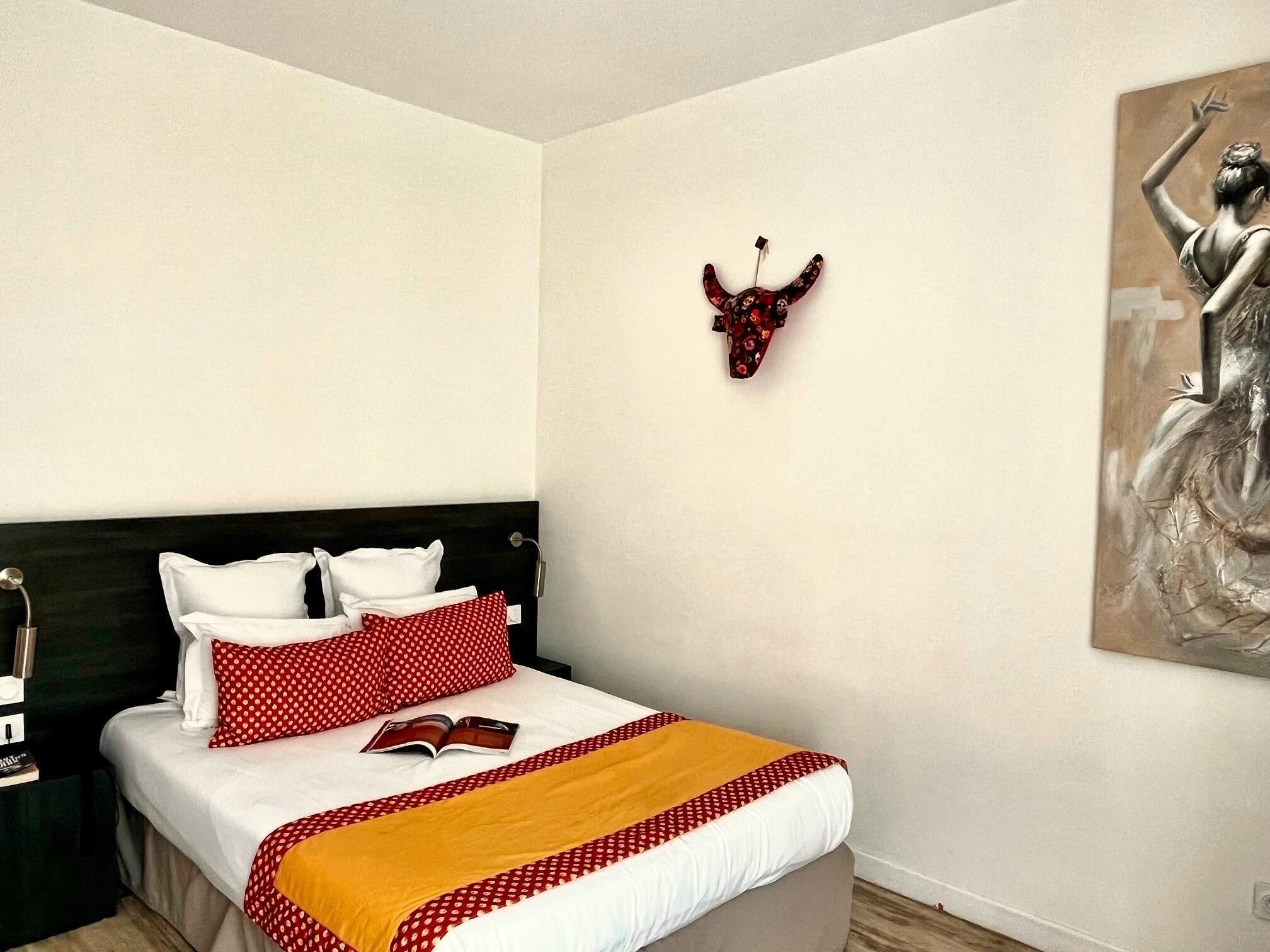 A neatly made bed with a red and white patterned blanket, white pillows, and a red polka dot pillow.