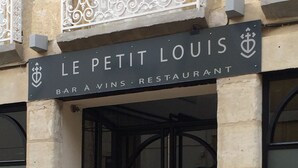 La entrada a Le Petit Louis, un bar y restaurante con puerta de vidrio y un letrero arriba.