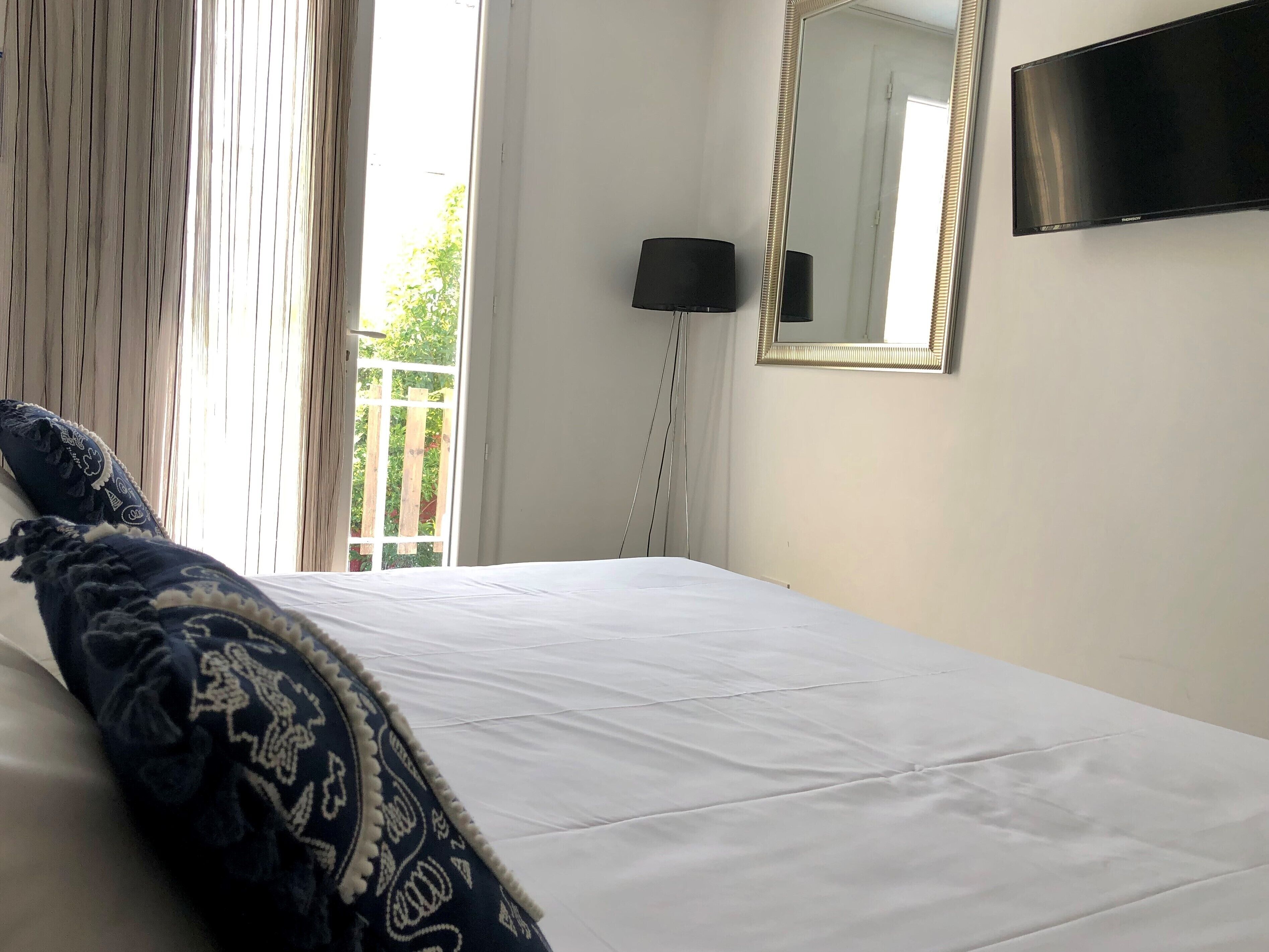 A bedroom with a bed, a large mirror, a flat-screen TV, and a window with curtains.