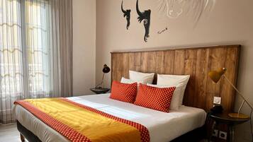 A hotel room with a wooden headboard, a bed with white and red bedding, a bedside lamp, and a wall art piece.