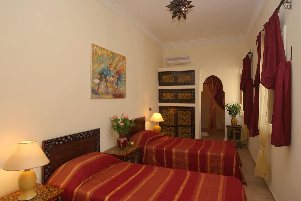 A hotel room with two beds, a painting on the wall, an air conditioning unit, and a decorative lamp.