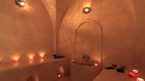 Una habitación abovedada tenuemente iluminada con una bañera, velas y objetos personales en estantes.