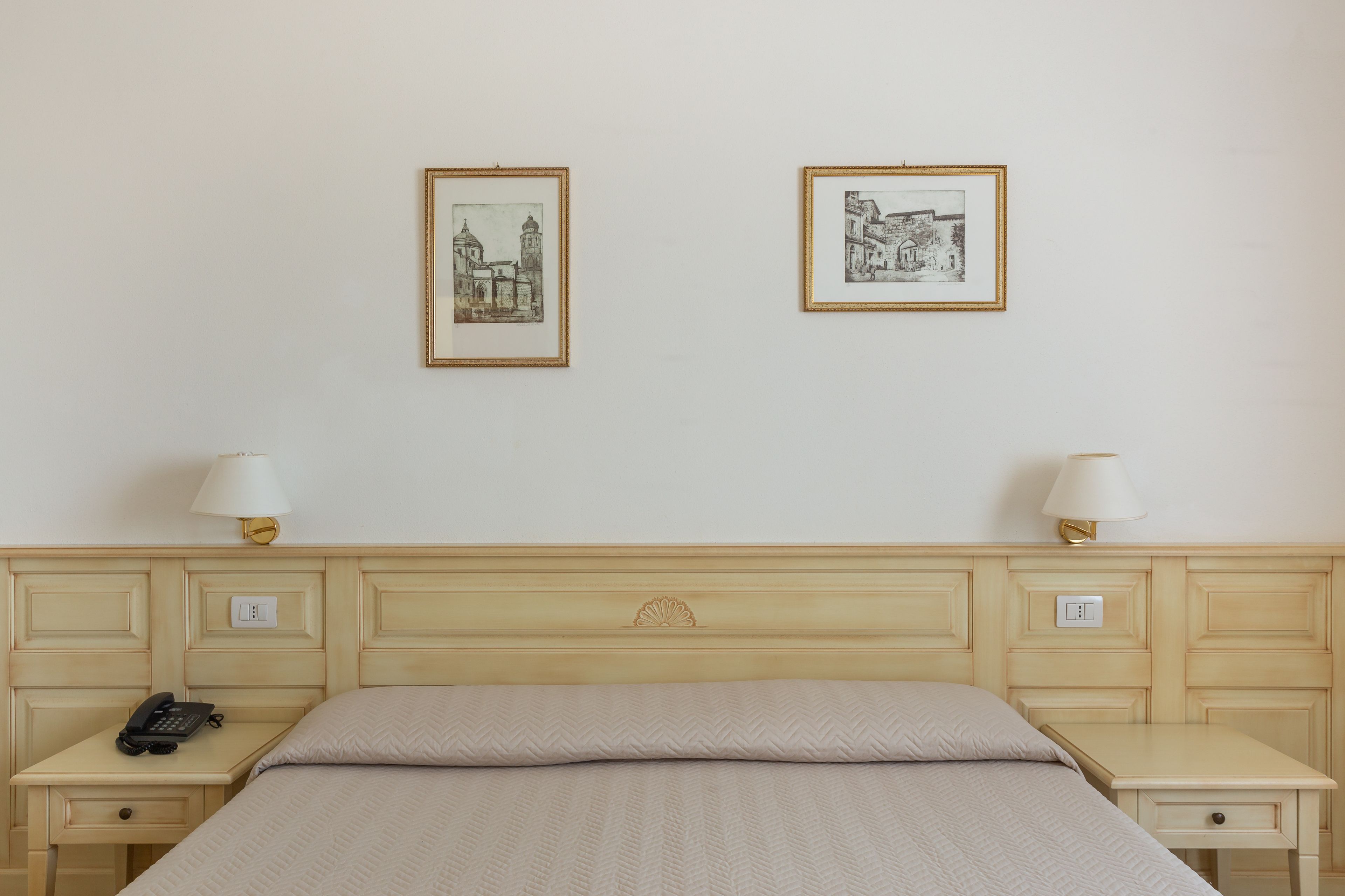 Una camera d'albergo con un letto, comodini, lampade, un telefono e due quadri appesi al muro.
