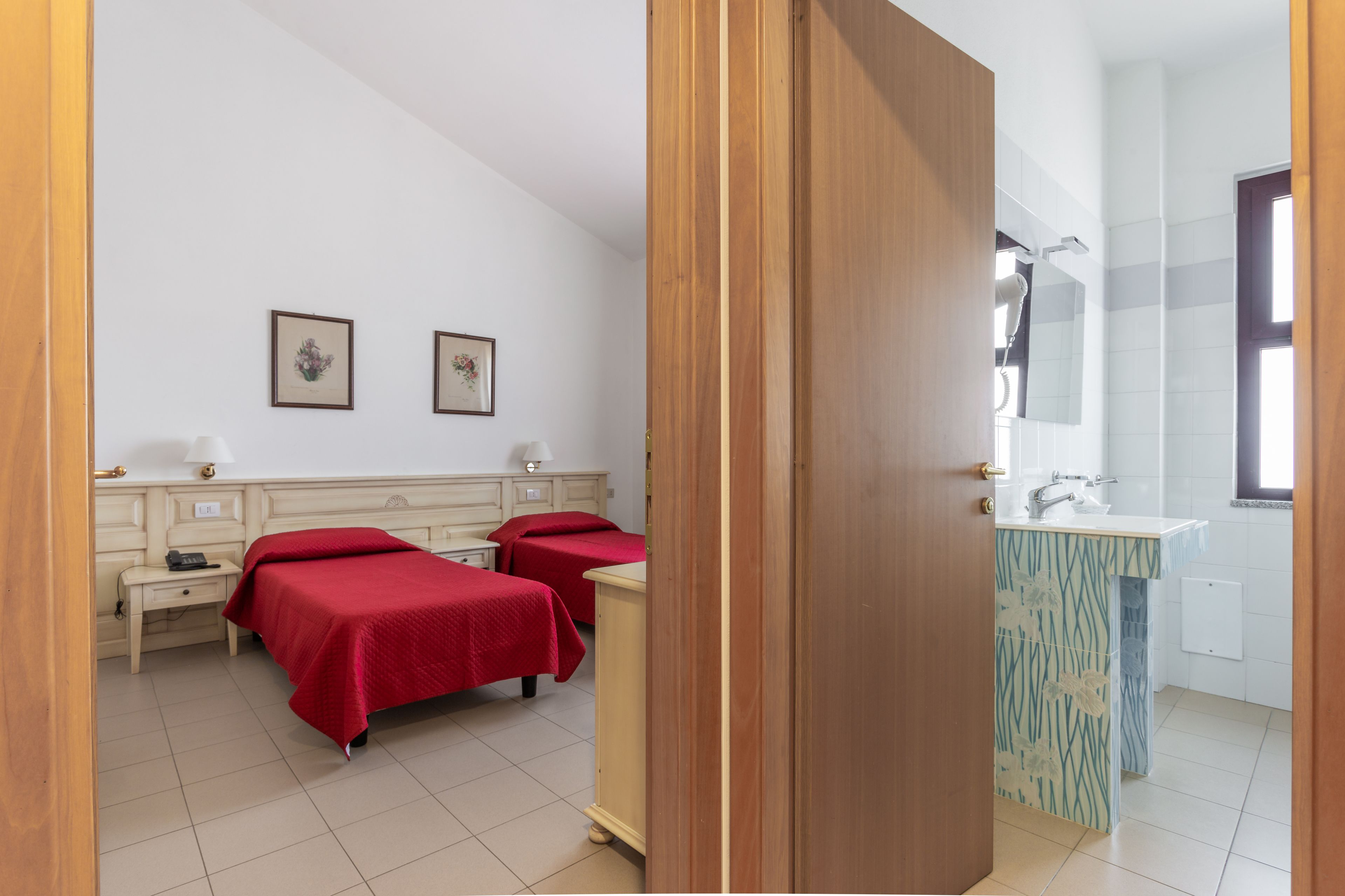 A hotel room with two beds, a bedside table, a nightstand, a bathroom with a sink and mirror, and a shower.