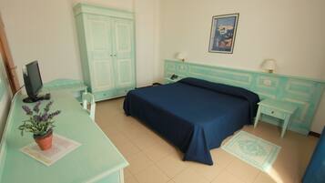 A room with a bed, a desk with a computer, a wardrobe, and a small table with a lamp.