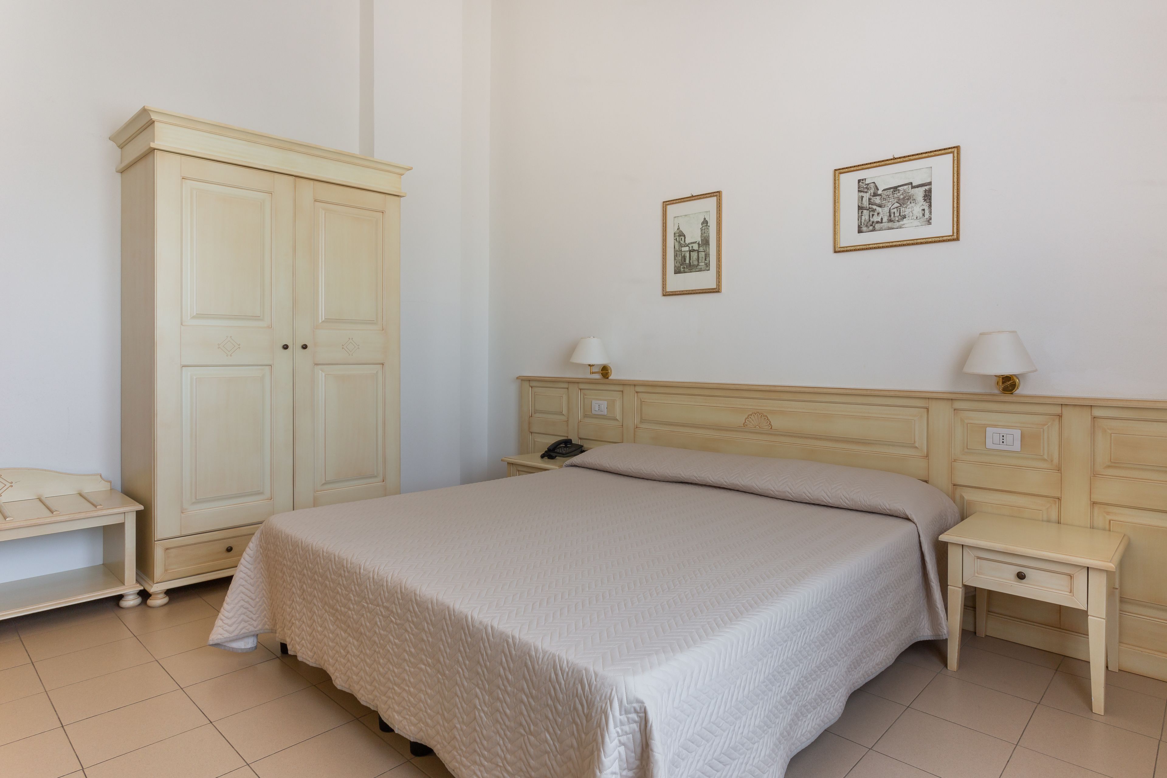 A bedroom with a large bed, a wardrobe, bedside tables, and two framed pictures on the wall.