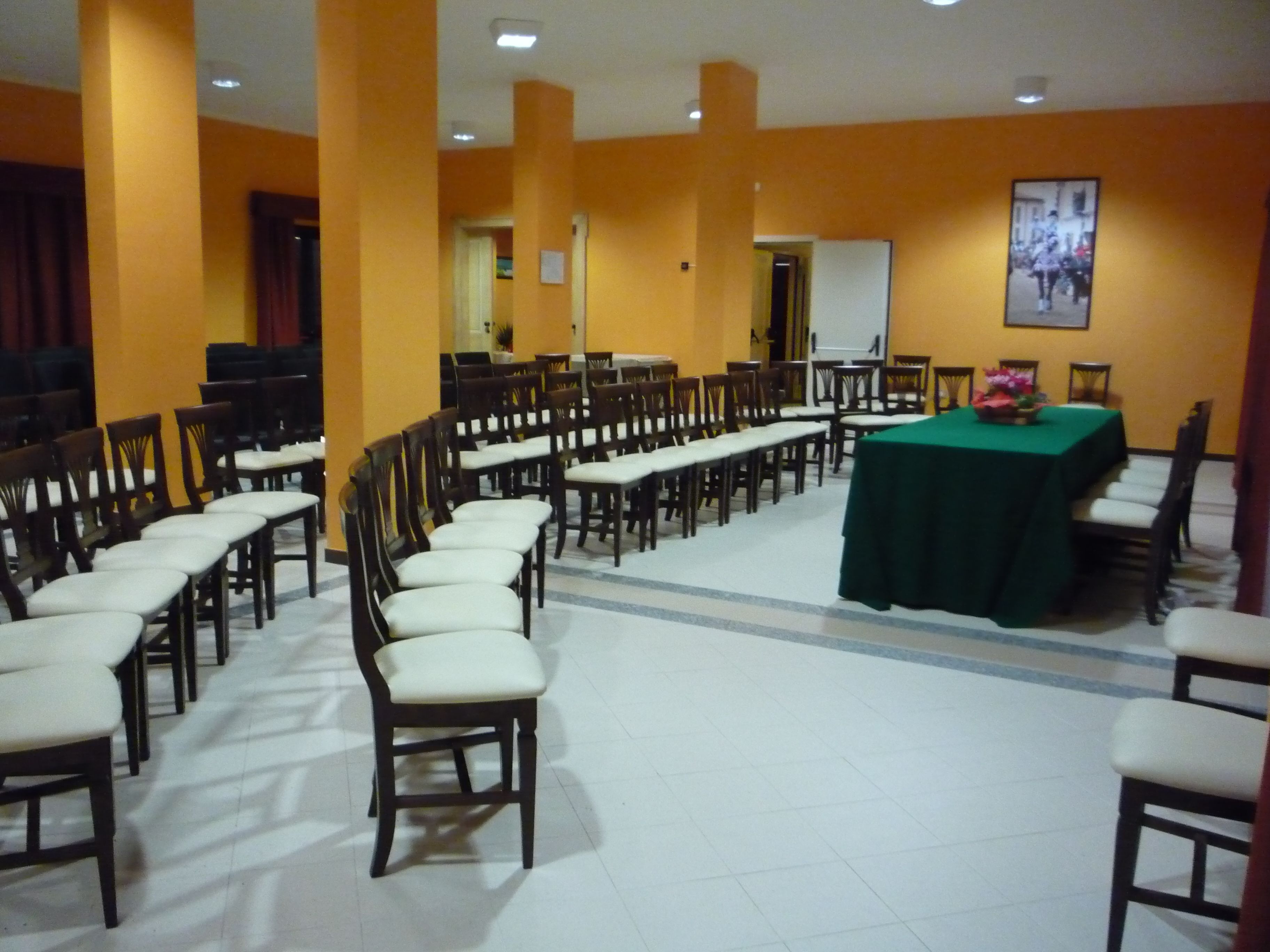 Une salle de conférence avec des rangées de chaises en bois et une table recouverte d’une nappe verte.